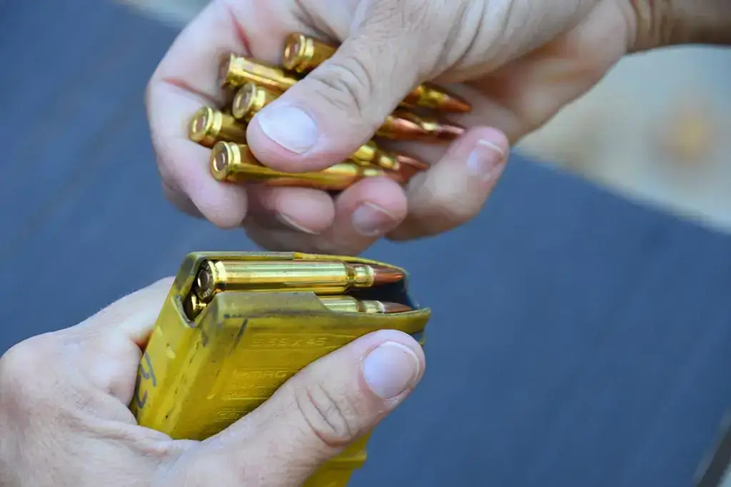 A lifestyle shot of a shooter loading a magazine with high-quality brass rounds at a range